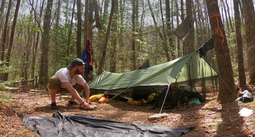 A person sets up their tarp shelter in a wooded area as part of the Solo experience. 